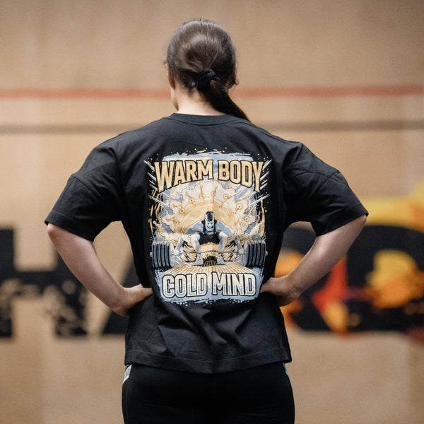 Person wearing a сotton black T-Shirt Lift Off with a graphic design and text on the back, standing in an indoor setting – Warm Body Cold Mind